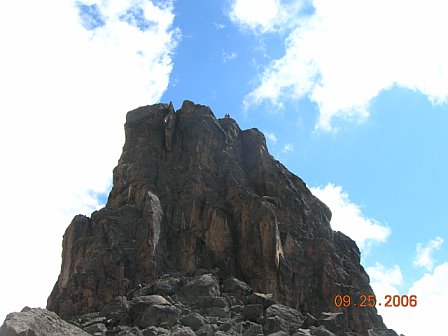Majestic mountain peak with rugged rocky surface under a bright blue sky with clouds, captured during a Kilimanjaro expedition.