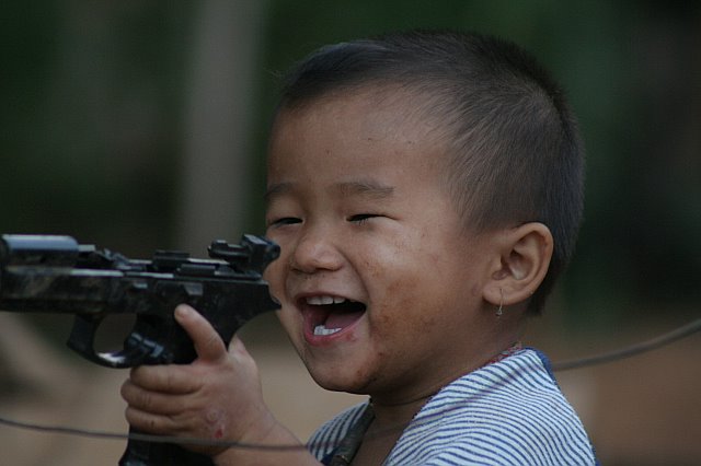 Young boy smiling and playing with a toy gun outdoors in Chiang Mai, Thailand, during an adventure trip.