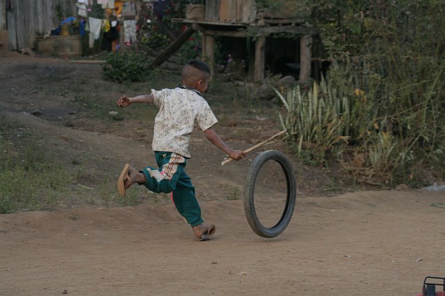 Young boy in Chiang Mai playing with a tire on a dirt road, showcasing local childhood activities and rural environment.