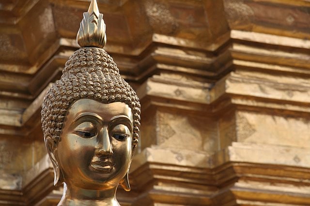 Close-up of a golden Buddha statue with intricate details, set against a background of traditional Thai architecture in Chiang Mai.