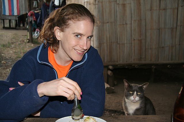 A woman smiling at a cat while dining outdoors in Chiang Mai, Thailand, during a nighttime adventure.