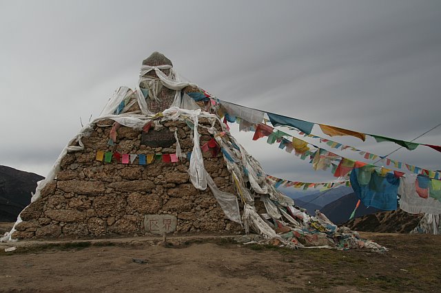 Ancient stone stupa decorated with colorful prayer flags and cloths in a remote mountain landscape.