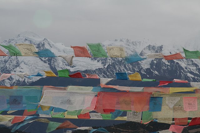 Colorful prayer flags fluttering against snow-capped mountains in a remote landscape.