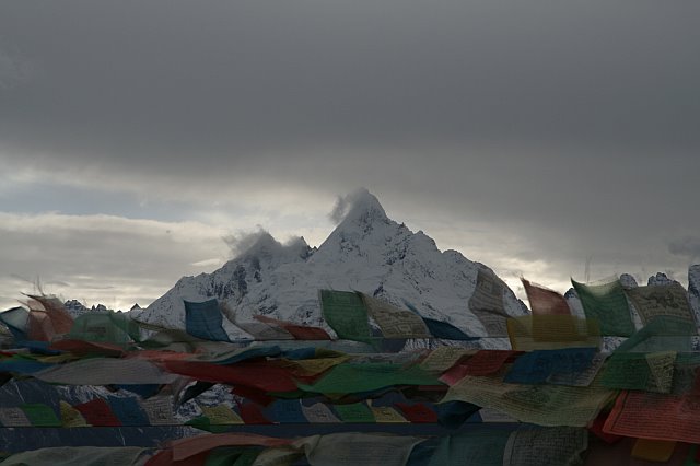 Snow-capped mountain with prayer flags fluttering in the wind under a cloudy sky.