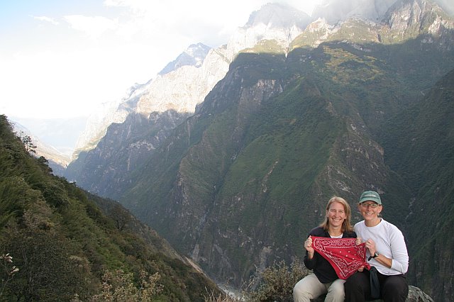 Two travelers with a red bandana in front of towering green mountains at Tiger Leaping Gorge.