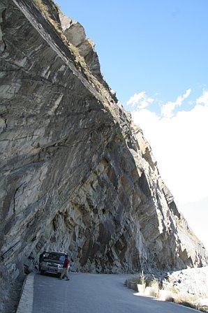 Scenic view of a winding mountain road through a massive rocky gorge with a vehicle parked along the edge.