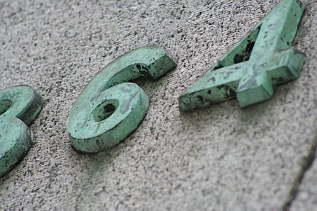 Close-up of weathered green numbers 64 and 74 mounted on a textured wall, emphasizing their aged appearance and historical significance.
