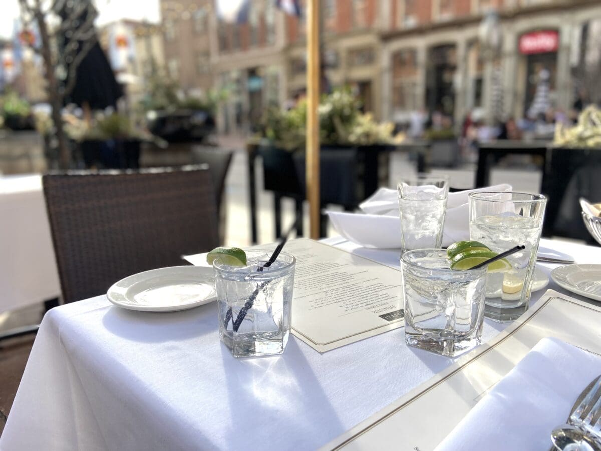Table covered with white linens and holding two cocktails with view of Larimer Street