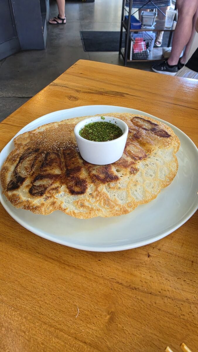 Large crispy quesadilla served with a side of green salsa in a small white bowl on a wooden table.