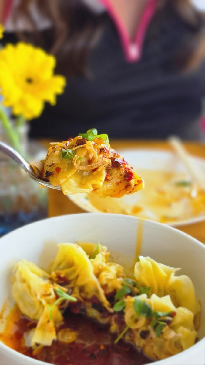 Close-up of a fork lifting a slice of cheesy, vegetable-filled casserole with a person in the background.