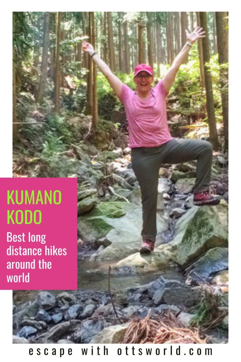 A woman hiking in a lush forest, balancing on rocks with arms raised in excitement, wearing a pink hat and shirt, promoting Kumano Kodo long-distance hikes worldwide.