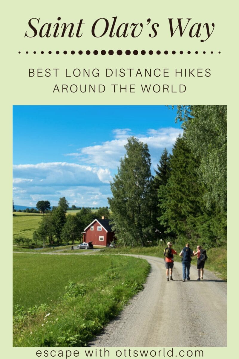 A lush green countryside with a red barn, a winding dirt path, and three hikers enjoying a scenic long-distance hike in a rural setting.