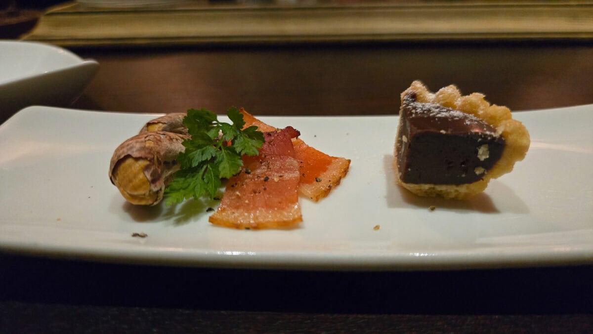 Elegant Japanese dessert plate with a chocolate tart, smoked salmon, and garnished with fresh herbs, served on a white rectangular dish.