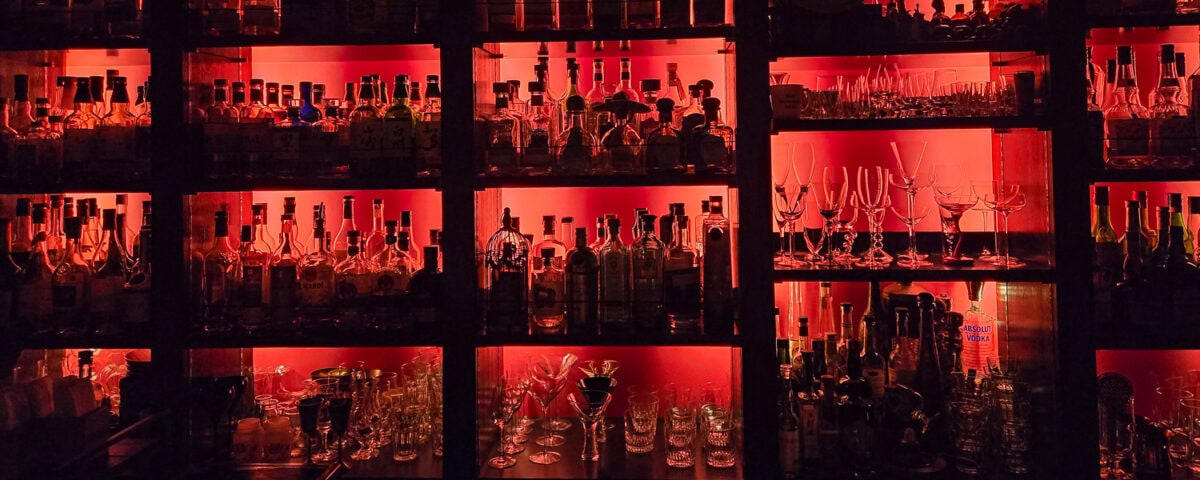 Bar shelves illuminated with red lighting showcasing various bottles and glassware for a stylish nightlife setting.