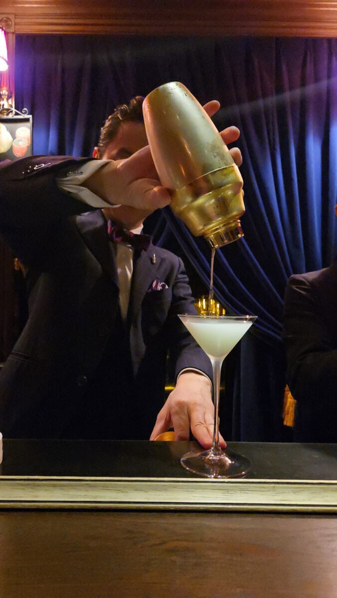 Bartender pouring a cocktail from a gold bottle into a martini glass at a Japanese shot bar.