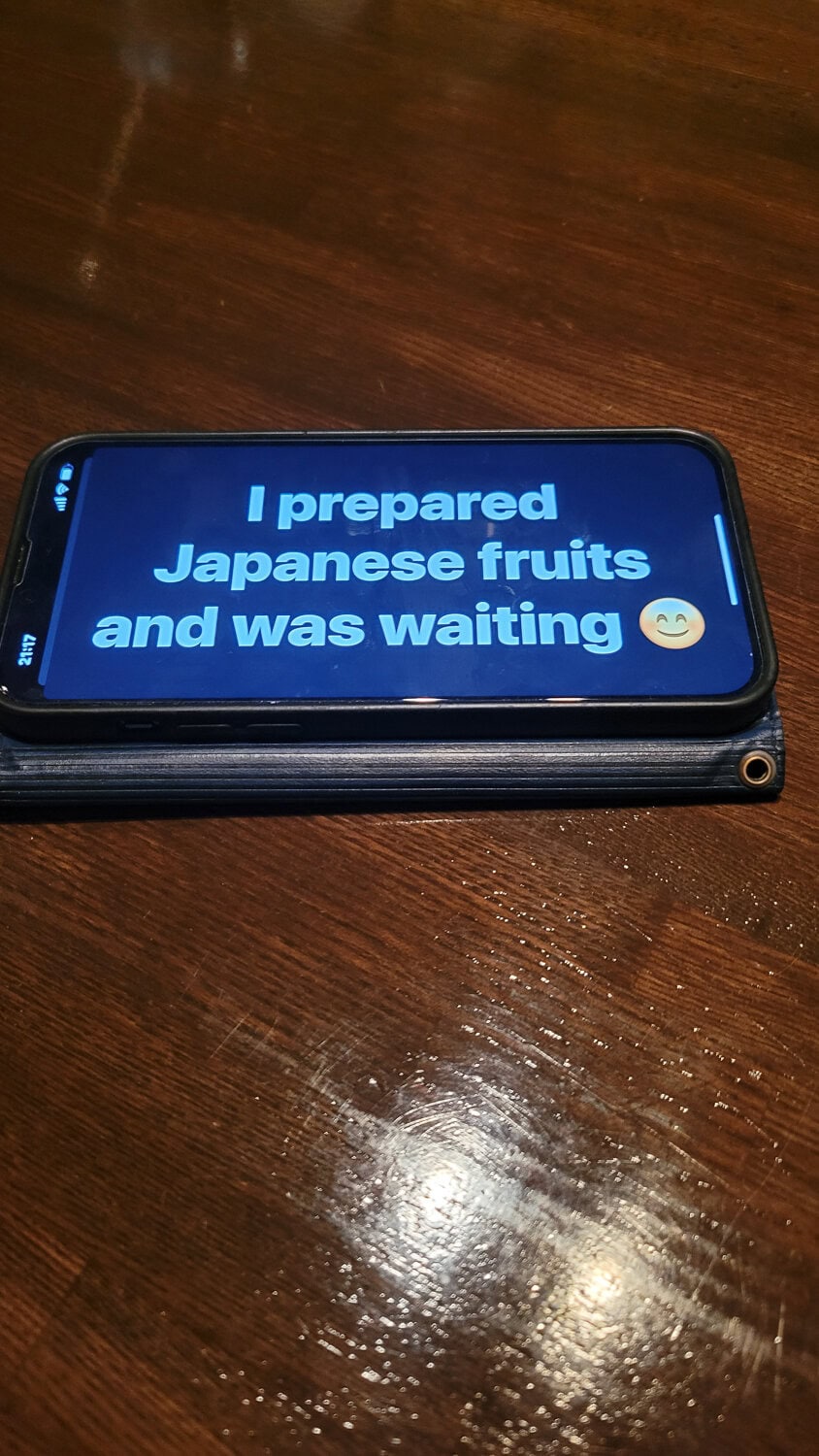 Smartphone screen displaying a message about Japanese fruits with a smiling emoji, on a wooden table.