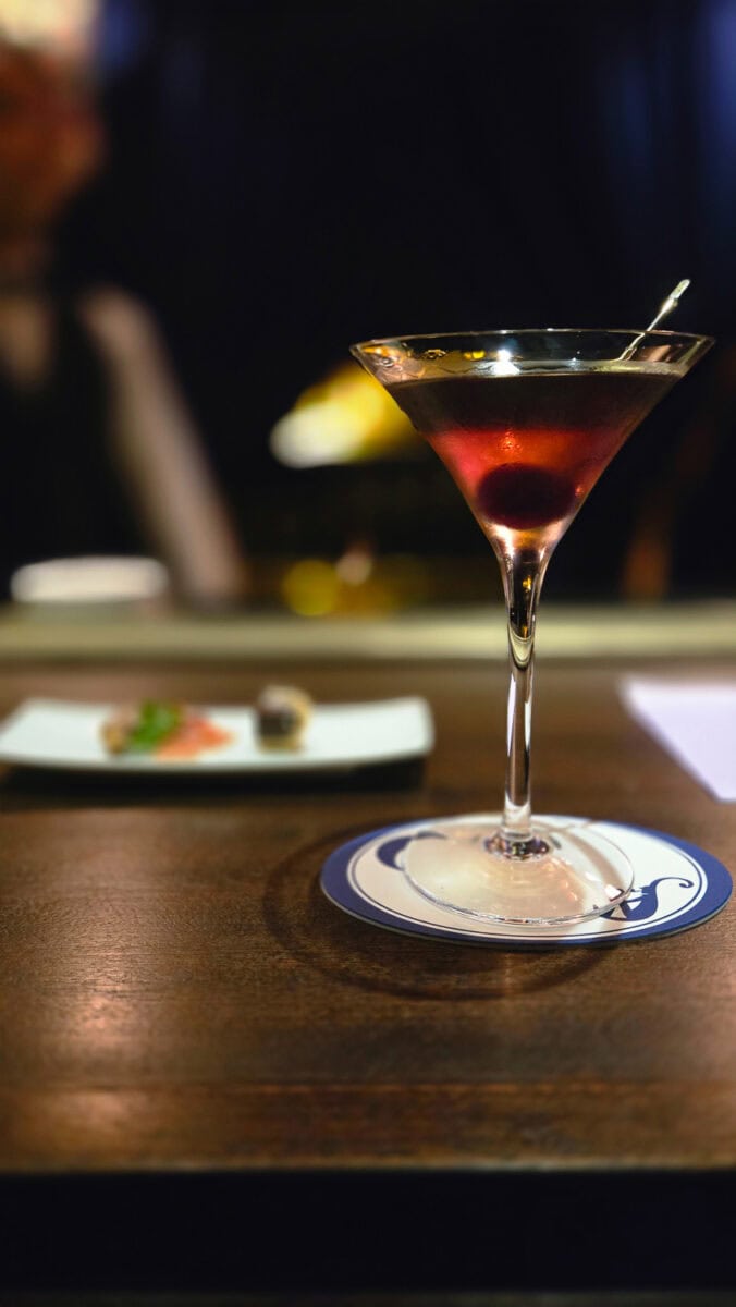 Elegant cocktail in a martini glass on a bar counter with a blurred background of a bar setting.