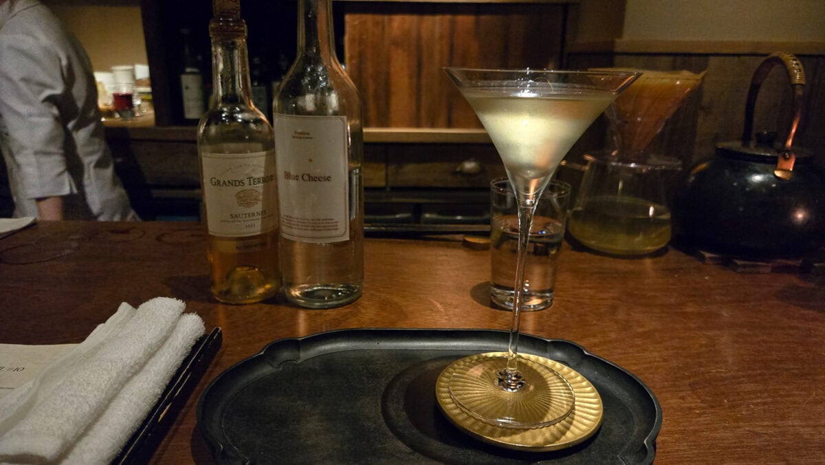 Elegant cocktail served in a martini glass on a wooden bar counter with bottles and bar tools in the background.