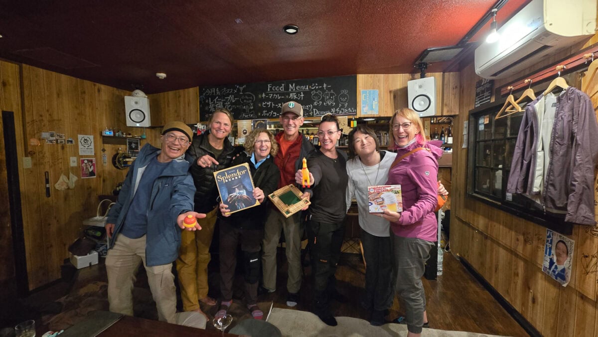 Group of seven diverse travelers enjoying a food and drink experience at a cozy, wood-paneled restaurant or bar, smiling and holding food and drink items.