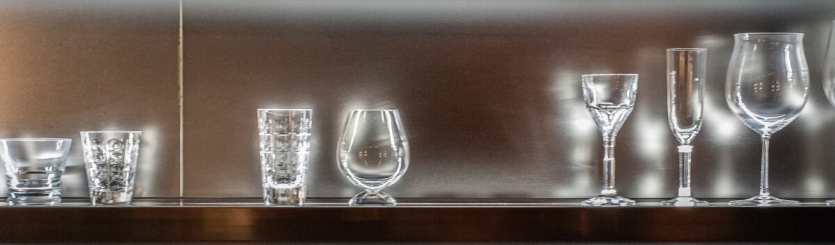 Collection of various glassware including shot glasses, tumblers, wine glasses, and champagne flutes displayed on a wooden surface.