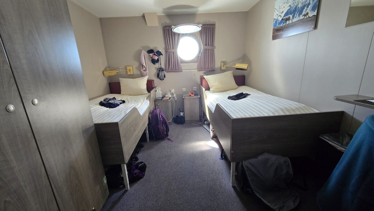 Cozy cruise ship cabin with two beds, window, and personal belongings, offering comfortable accommodation for Antarctic travelers.