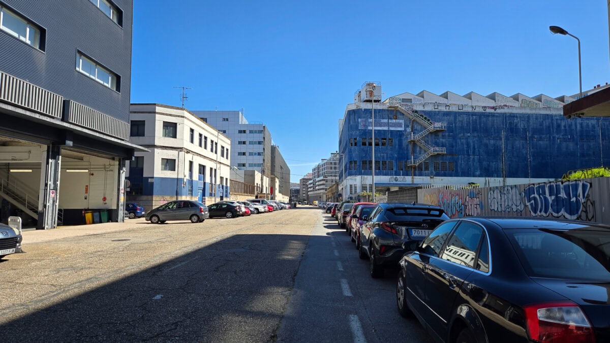 Urban street scene with parked cars, modern buildings, and a clear blue sky in a city environment.