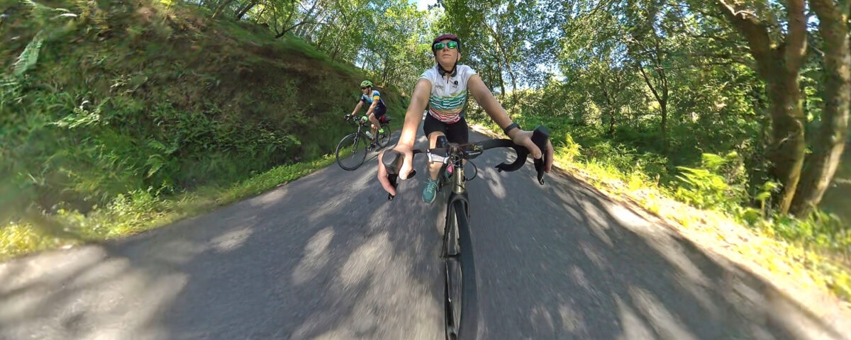 Cyclists riding mountain bikes on a shaded forest trail during daytime, enjoying outdoor adventure and nature.