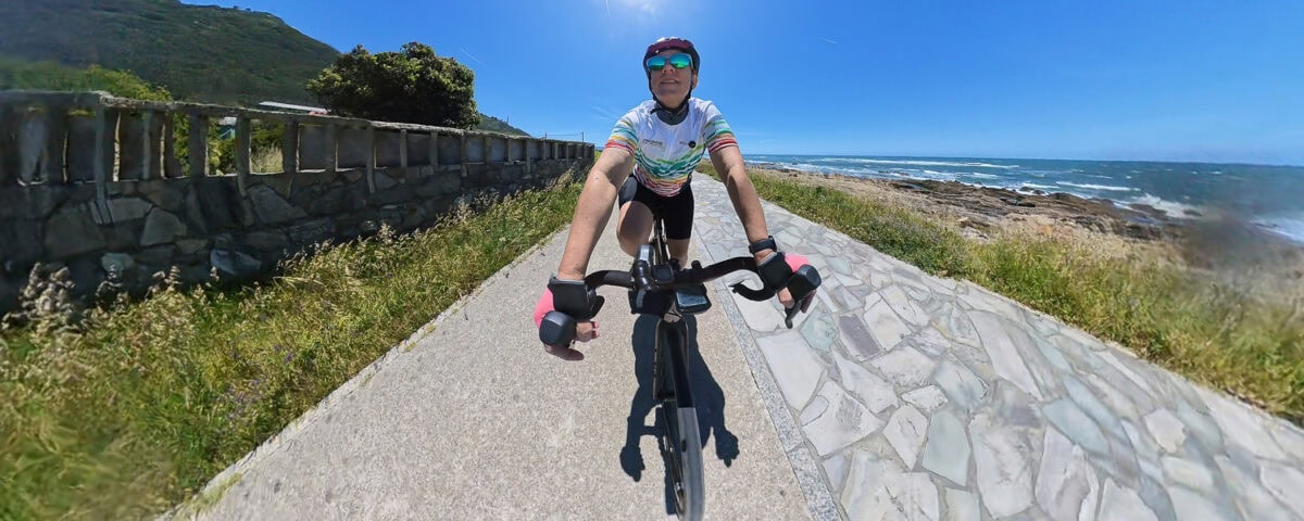 Woman cycling along a scenic coastal path with ocean views and lush greenery on a sunny day.