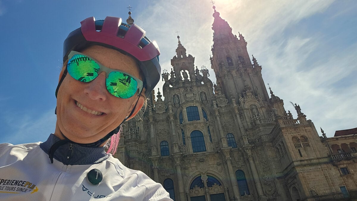 Smiling cyclist wearing helmet and sunglasses in front of historic cathedral during daytime.