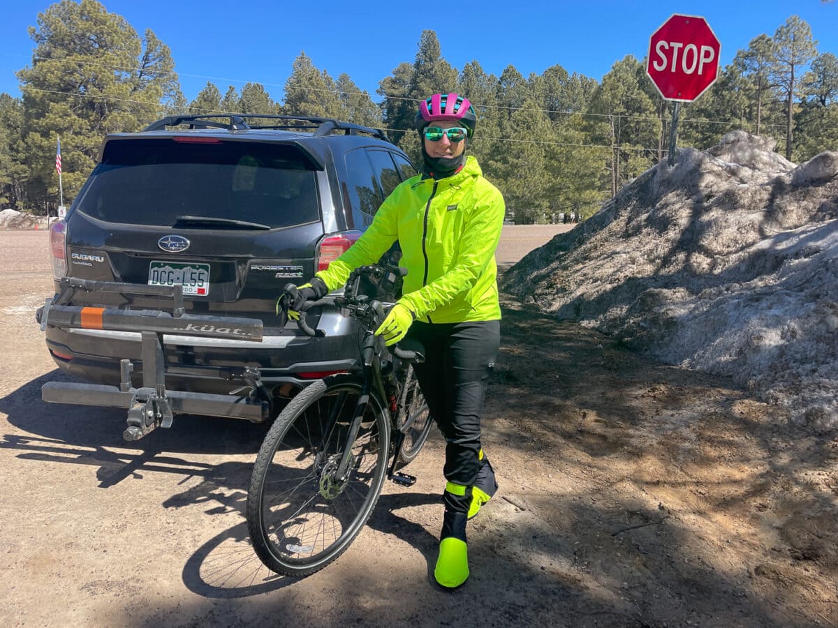 Cyclist in bright yellow gear with helmet and sunglasses standing with bike near stop sign and rocky terrain.