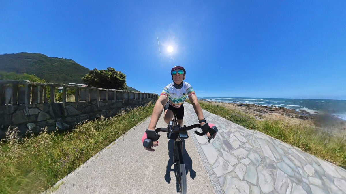 Cyclist riding along a coastal path on a sunny day, with clear blue sky and ocean view in the background.