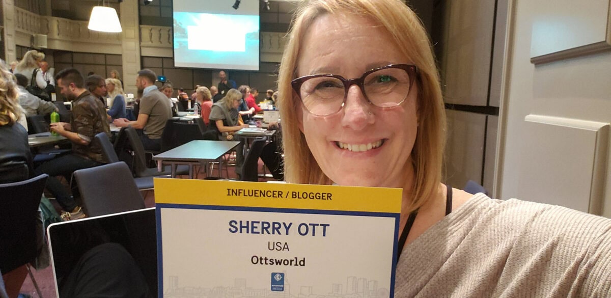 Smiling woman with glasses holding a Sherry Ott influencer badge at a conference.